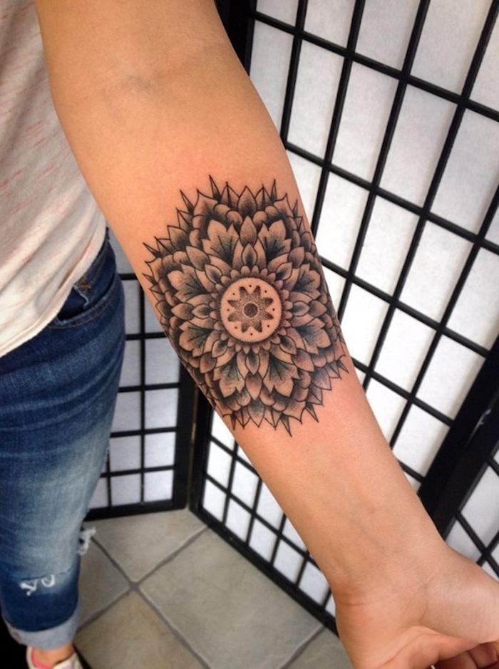 Mandala tatouage sur l'avant bras, femme jean long et t-shirt blanche, dessin de fleur lotus mandala