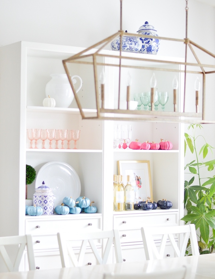 decoration avec potirons citrouilles repeintes de couleur violette, bleue et rose sur vaisselier blanc, table et chaise blanche