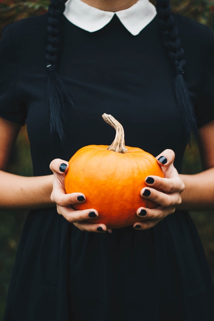 photo halloween de jeune fille déguisée en sorcière habillée en robe noire avec ongles noirs et citrouille symbole Halloween