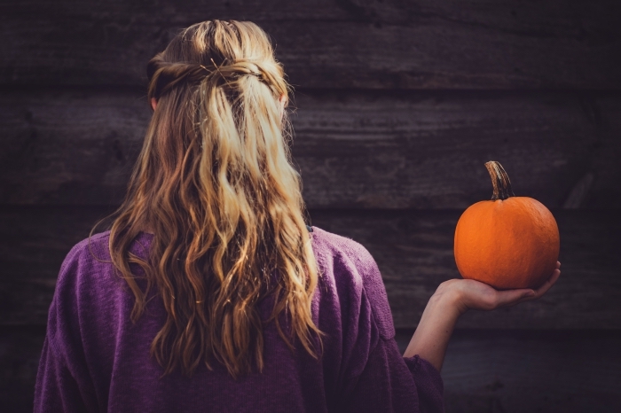 déguisement-femme-en-sorcière-halloween-citrouille-façade-maison-hantée-en-bois-coiffure-cheveux-longs-mi-attachés comment s'habiller pour Halloween femme, idée déguisement fille en sorcière aux cheveux longs avec citrouille dans la main