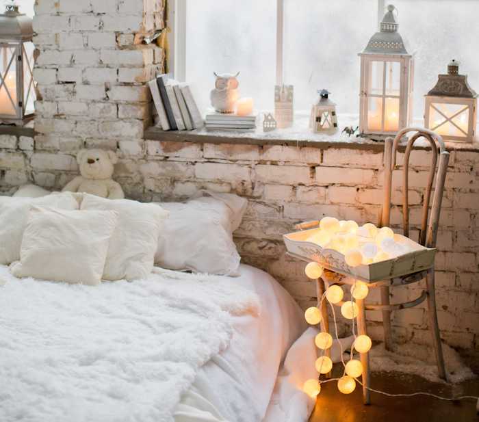 deco loft industriel romantique d hiver, chaise bois brut avec guirlande boule, linge de lit blanc avec peau de mouton blanche, deco rebord de fenetre en lanternes, livres et figurines decoratives
