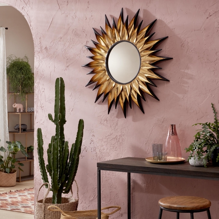 modèle de miroir soleil doré avec rayons à pointes noires, décoration salon exotique aux murs rose pastel avec plantes vertes