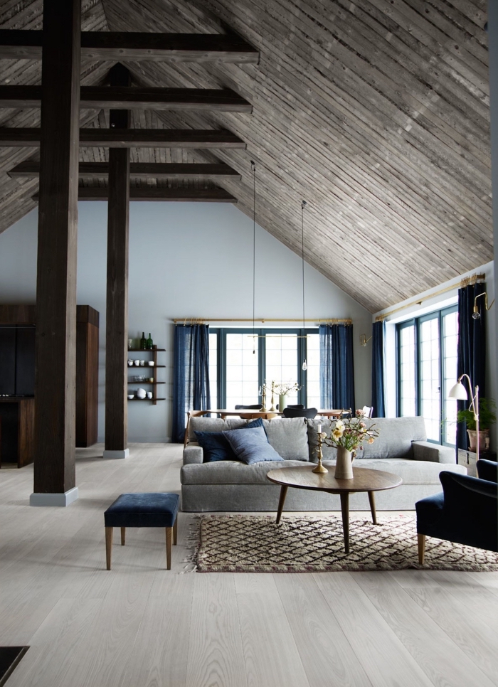 projet transformation grange en habitation, décoration salon loft aux murs blancs avec plafond bois foncé et meubles gris et bleu marine