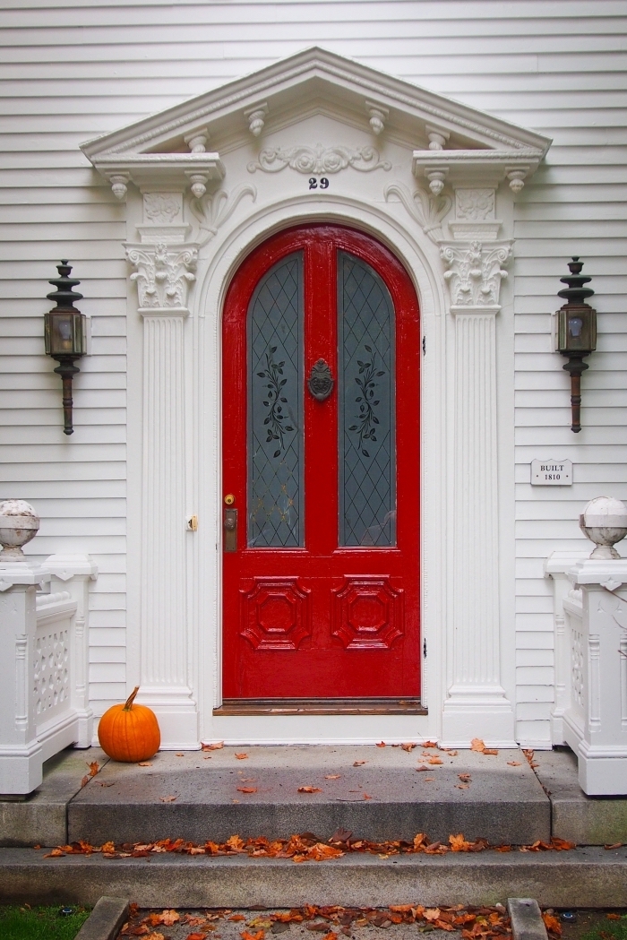 porte-rouge-façade-maison-blanche-ornements-plâtre-lanternes-halloween-2019-citrouilles-feuilles-séchées-maison-hantée wallpaper portable pour halloween avec photo de maison à façade blanche et porte rouge à décoration citrouille