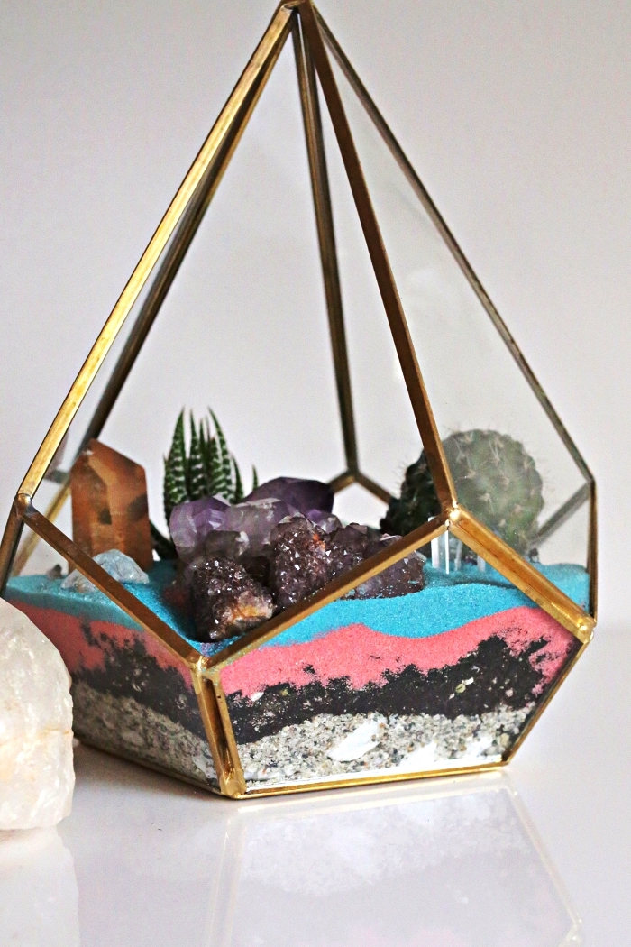 terrarium géométrique rempli de couches de sable couleur rose et bleu et décoré de cristaux