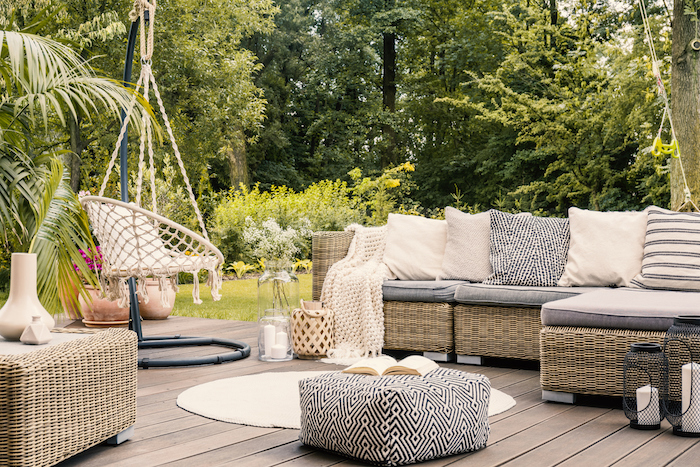 Salon de jardin design confortable, canapé d'angle en rotin, coussins cosy, balançoire dans le jardin, tapis rond