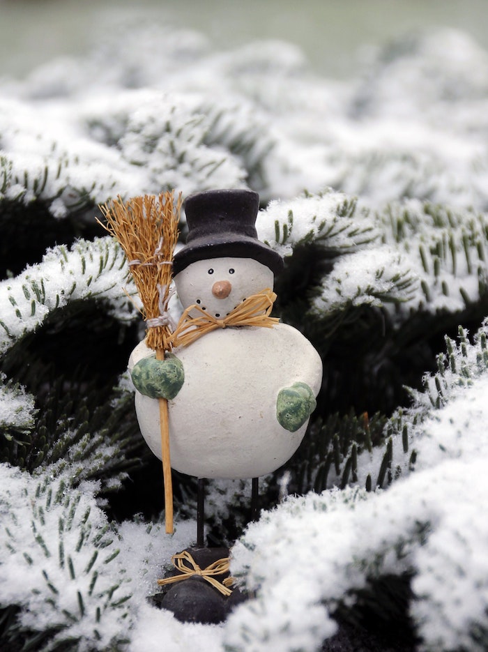 figurine bonhomme de neige en porcelaine sur branchage vert de sapin enneigé, belle image pour fond ecran
