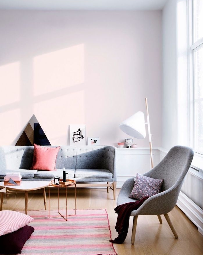 mur rose clair dans un grand salon gris, canapé et fauteuil gris, parquet bois clair, tapis à rayures coloré, amenagement salon cocooning