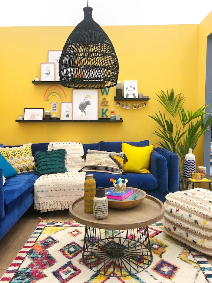 couleur mur salon jaune, canapé d angle bleu roi tapis coloré à figures géométriques, suspensions noires, parquet bois, coussins vert, jaune et blanc