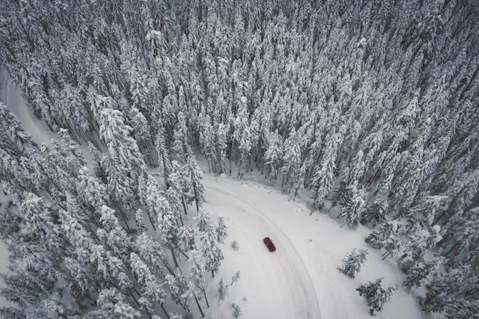 paysage de noel dans une foret aux pins avec un chemin enneigé qui passe à travers et voiture rouge, image vue d en hut