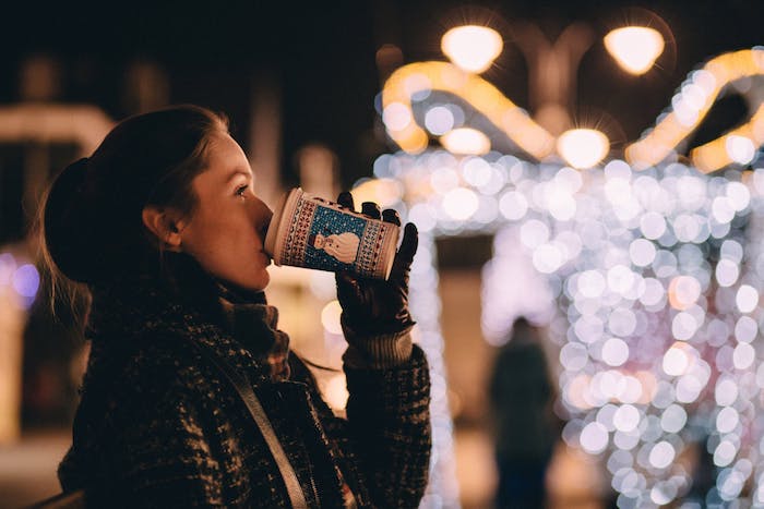 fond ecran noel avec lumières de noel et femme qui boit boisson chaude dans un gobelet bonhomem de neige