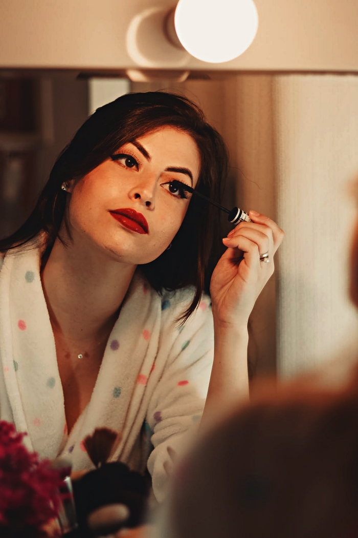 une jeune femme appliquant du mascara devant le miroir, conseils pour se maquiller les yeux sensibles, les meilleurs mascara pour pour yeux sensibles