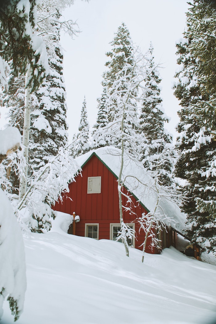 maison canadienne couleur rouge ensevelie sous la neige, plusieurs sapins enneigés et couche épaisse de neige