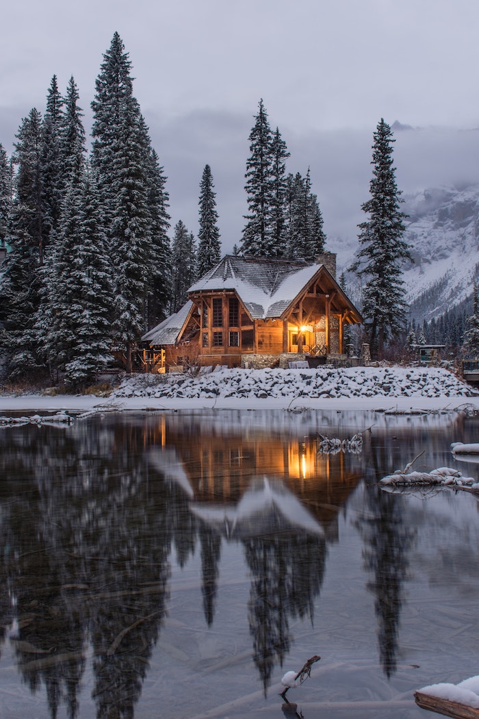 maison en bois style chalet de montagne aux eaux glaciales et des sapins de tailles variées, fond de montagnes en brume