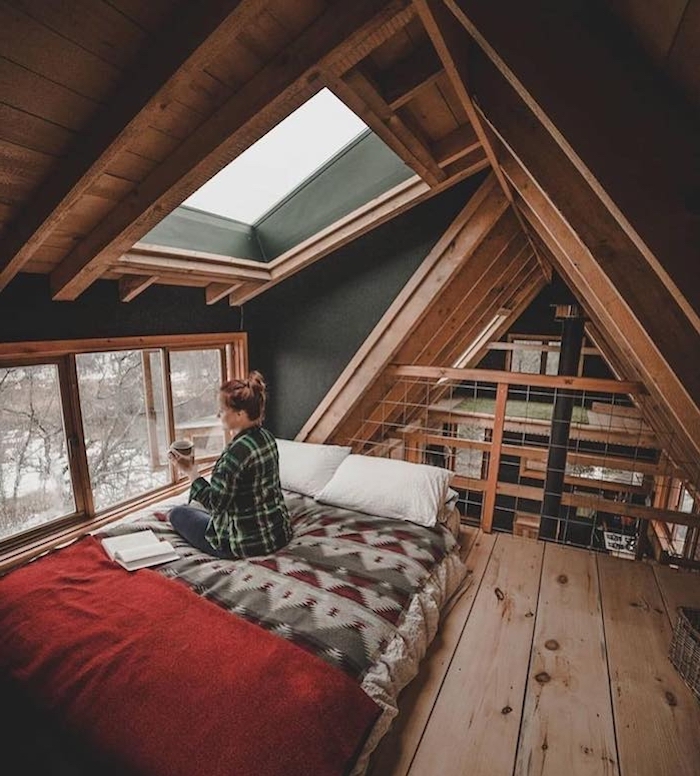 Femme assise sur son lit avec un livre et une tasse de café, deco chalet montagne, décoration scandinave en bois
