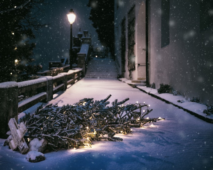 arbre de noel aux guirlandes lumineuses renversée dans une rue enneigé, paysage urbain triste nocturne