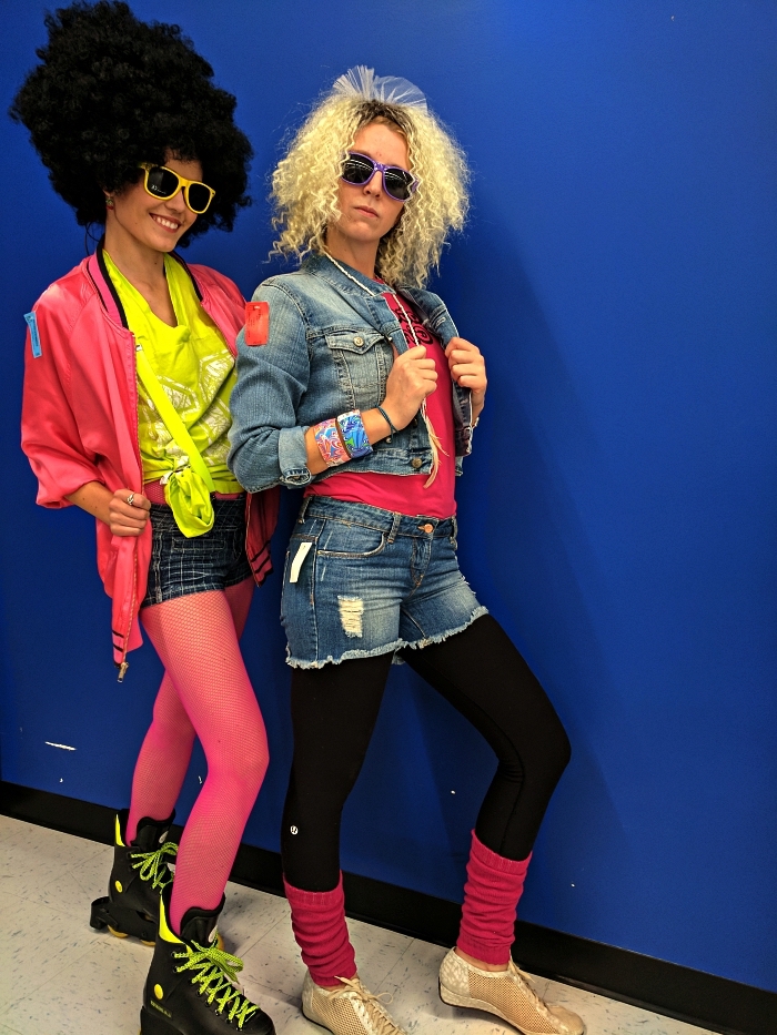 déguisement disco femme des années 80 composé de shorts, collant en résille rose, haut coloré et perruque de coiffure des années 80