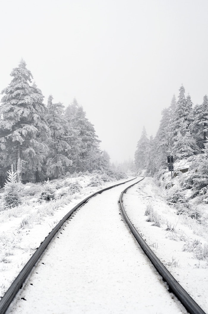  fond d'écran hiver, voie ferrée enneigée et des sapins enneigés des deux cotés, paysage montagnard avec neige et ciel blanchatre