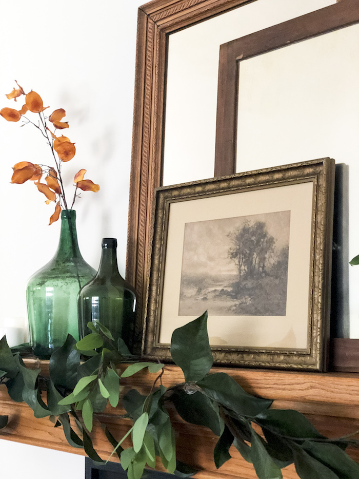 Verte vase dame jeanne, composition florale à faire soi meme, vase en verre avec fleurs oranges dedans et une branche feuilles vertes pour décorer l'espace au-dessus de la cheminée