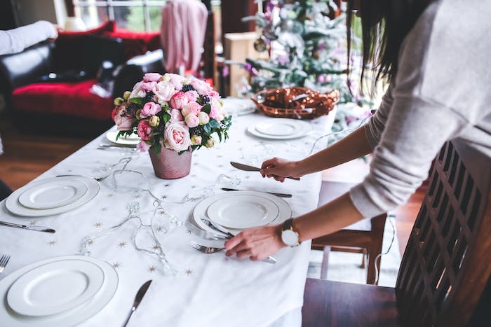 centre de table noel en bouquet de fleurs élégantes, guirlande lumineuse sur nappe blanche, assiettes blanches