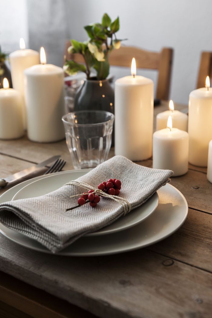 centre de table en bougies blanches de tailles variées, assiettes blanches avec serviette grise et houx rouge pour decorer
