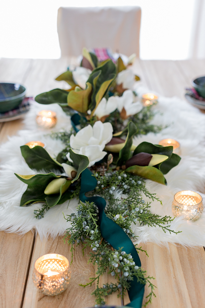 table de bois blond avec centre de table peau animale et composition florale de feuillages et fleurs blanches avec bougies aurour
