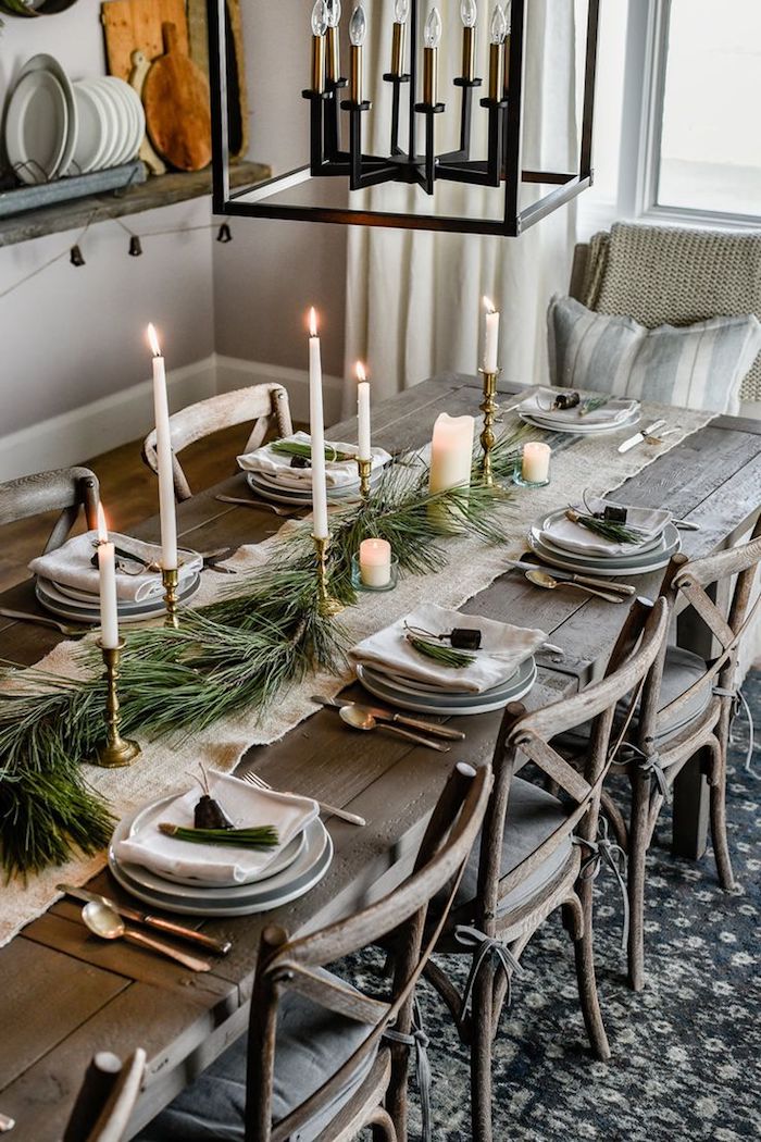 table bois brut style rustique avec des couverts dorés, assiette grises, marque place brins de pin, centre de table tissu gris et branches de pin, chandelles dorées, decoration de noel table