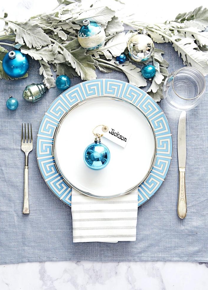 assiette bleu et blanc avec marque place en boule de noel bleue et centre de feuillages et boules bleues, comment dresser une table de noel