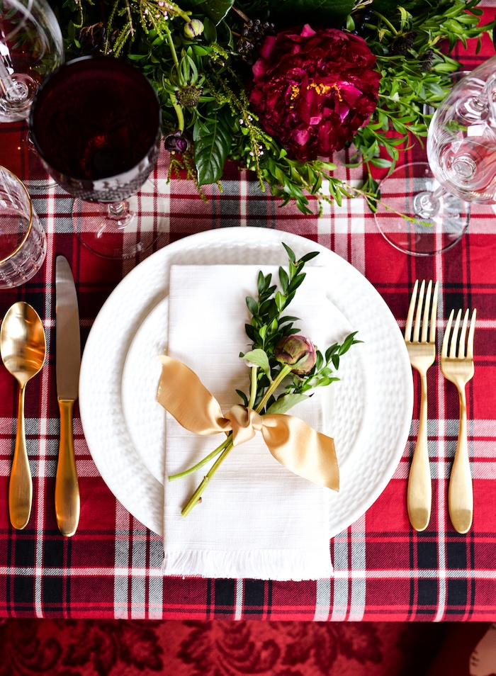 comment dresser une table de noel, jolie marque place végétale avec ruban doré, feuillage vert avec fleur rouge sur nappe rouge