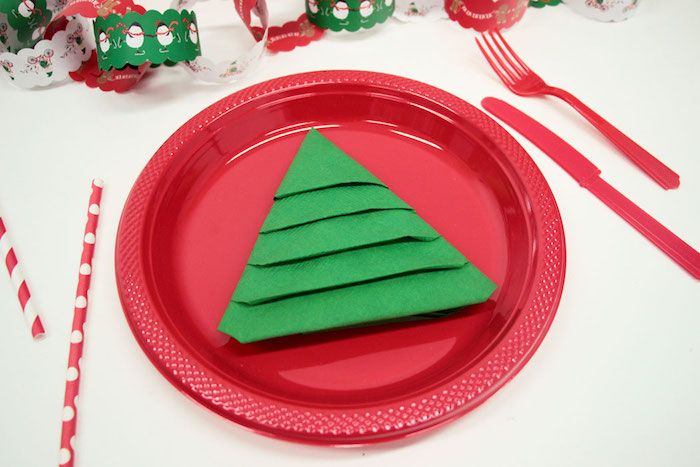 pliage de serviette sapin de noel en papier vert dans une assiette en plastique rouge et couverts de plastique, deco centre de table papier