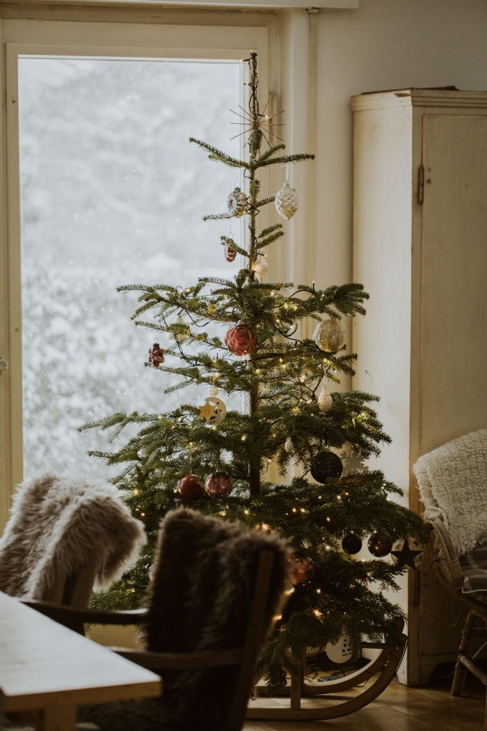 image noel 2019 avec un sapin naturel décoré d'ornements et guirlande lumineuse dans une salle de séjour avec chaise faux fur