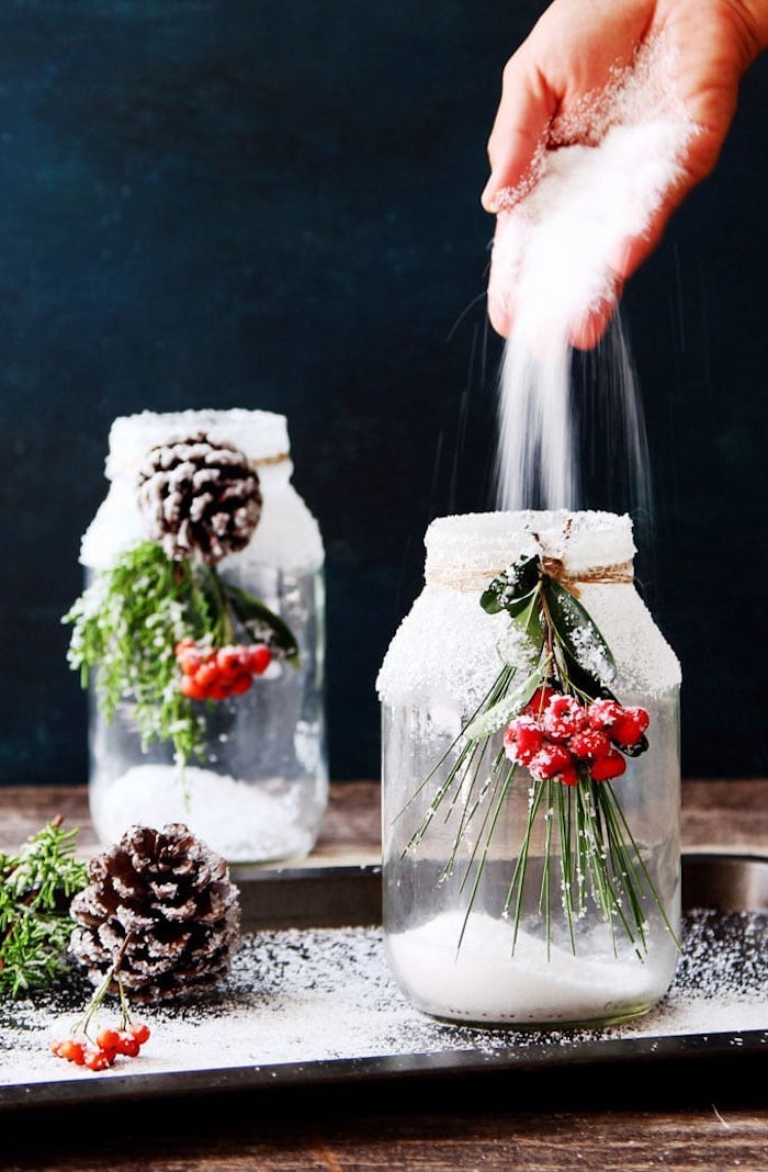 recyclage bocal en verre décoré de neige artificielle, noux et branches de pin dans un plateau de service noire, décoration de noel table
