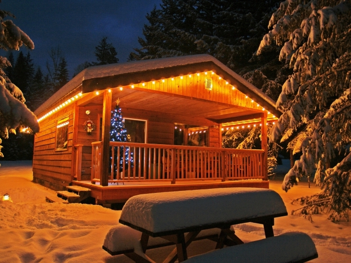 fond d'écran noel cocooning avec une cabane bois enneigée et sapin de noel décoré, photo de nuit de maison dans une montagne enneigée