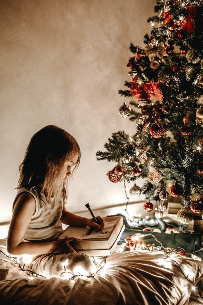 idée comment decorer un sapin avec ornements en rouge et or, photo de petite fille écrivant sa lettre au Père Noel