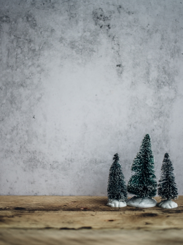 idée fond d'écran Noël minimaliste pour smartphone, photo de mini figurines d'arbres de Noël enneigés devant un mur bétonné