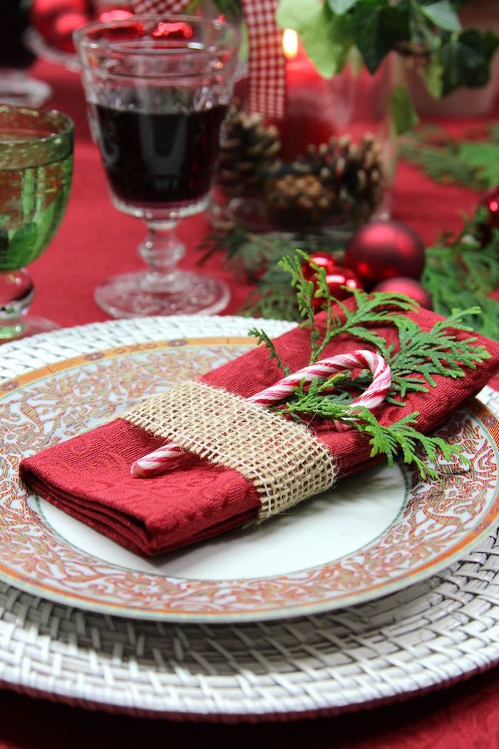 pliage de serviette rouge avec décoration de brin vert, canne de sucre, bande de jute, centre de table en verre avec pommes de pin
