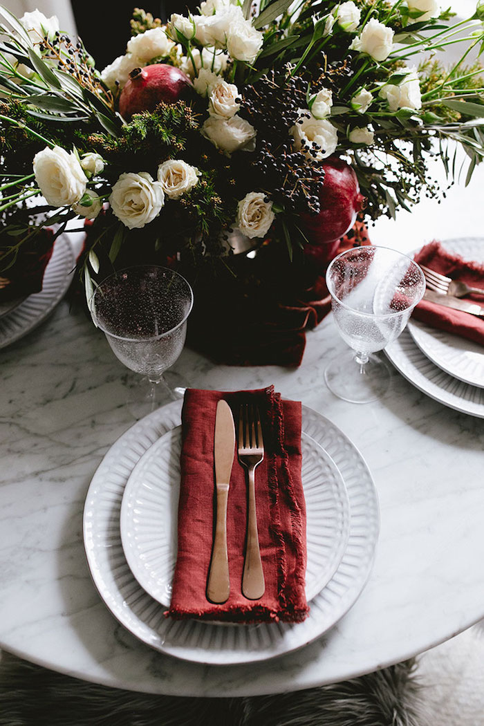 serviette en tissu rouge dans assiettes blanches, centre de table en bouquet de roses blanches avec grenade, deco table noel esthétique