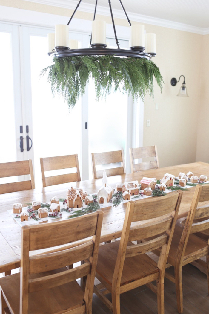 centre de table en tissu blanc décoré de maisons en pain d épice et des branches de pin autour, suspension originale en bougies et pin