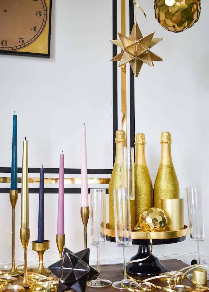 bouteilles de champagne en or et paillettes, bougies sur des chandelles dorés, suspensions originales au dessus d une deco festive