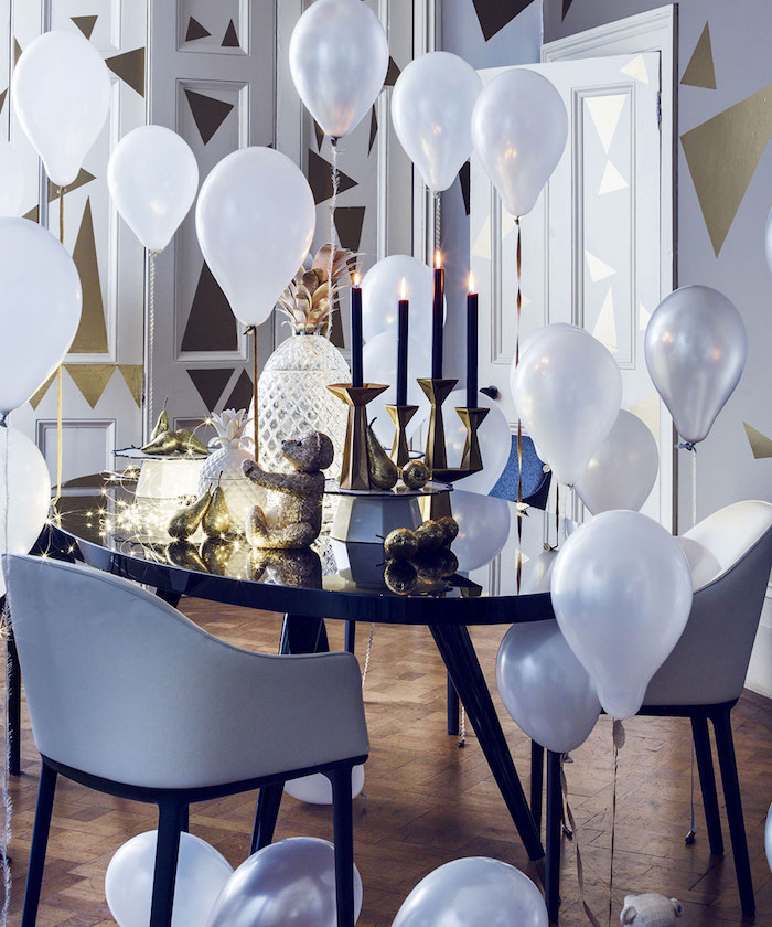 table noire, chandelles or avec bougies noires, guirlande lumineuse et ananas deco, ballons blancs et murs décorés de triangles dorés, theme nouvel an elegant