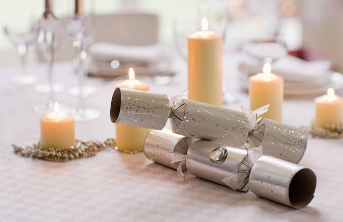 canons à confettis et guirlande de perles autour de bougies de taille variées sur nappe gris et blanc