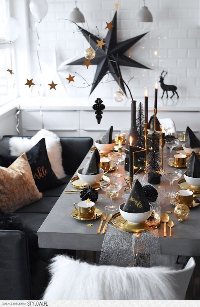 table grise avec couverts et assiettes or et blanc, bougies et accents deco noiors,, deco murale grande étoile noire, deco nouvel an stylée