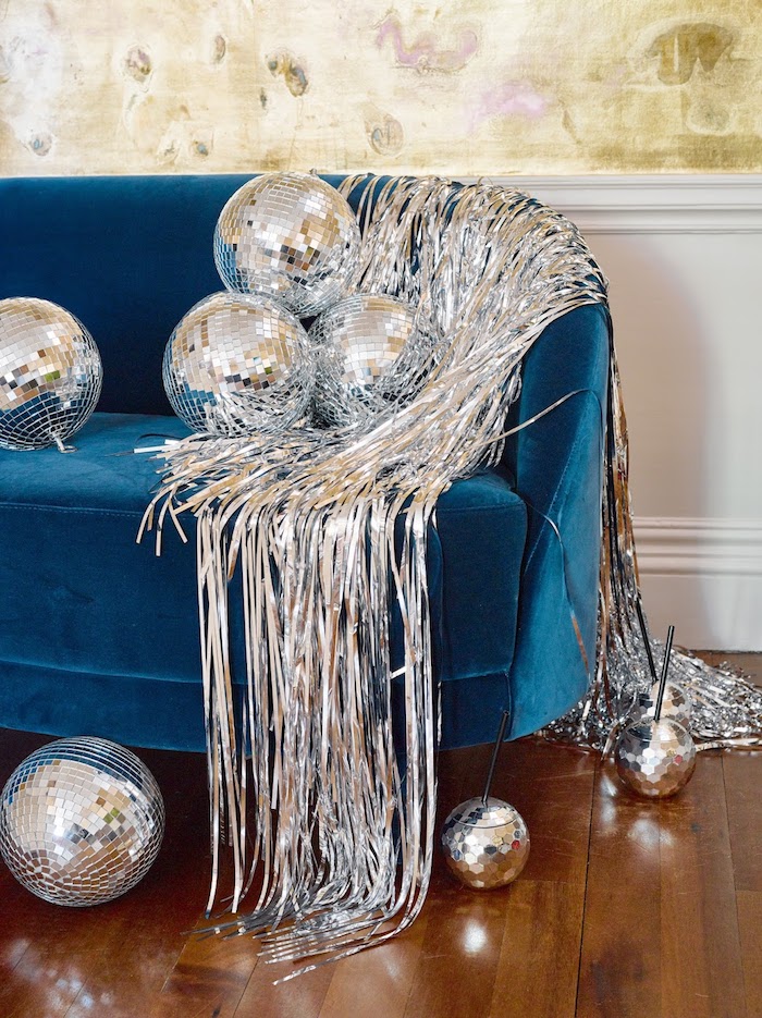 guirland argenté et des boules à facettes sur canapé bleu canard dans un salon cocooning décoré pour le jour de l an