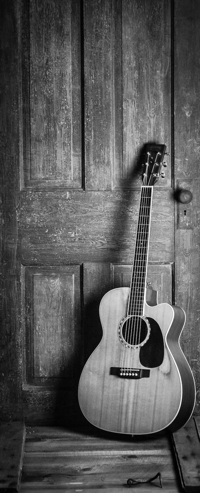 Guitare sur une porte d'entrée en bois, fond sombre, photo monochrome élégante à utiliser sur son portable