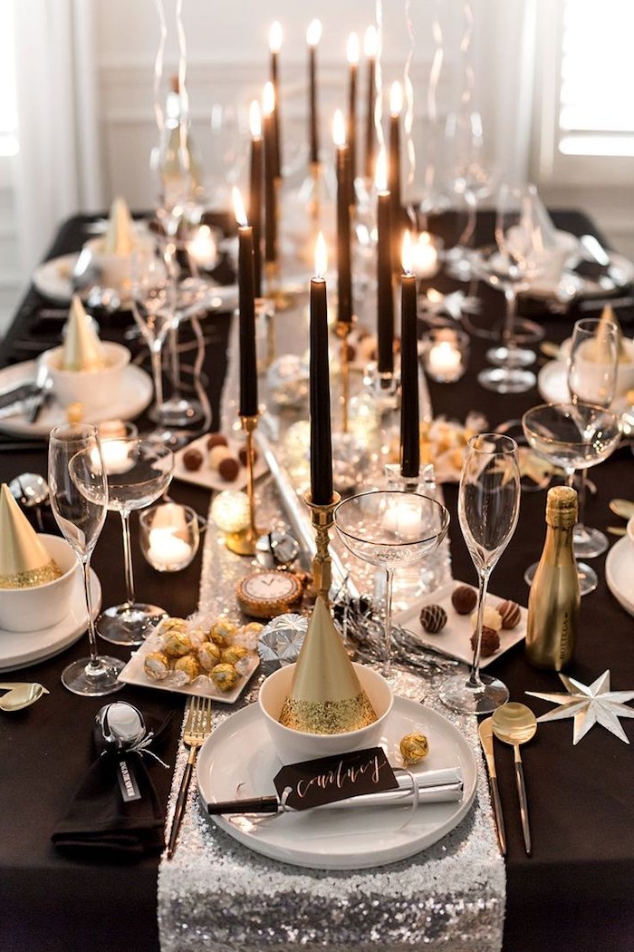 table décorée de nappe noire et chemin de table argenté, bougies noires sur chandelles or, deco noir blanc et or elegante