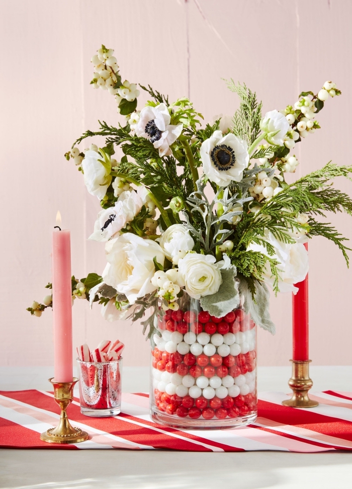 centre de table noel facile avec fleur, diy composition florale en blanc et vert dans un contenant en verre rempli de boules rouges et blanches