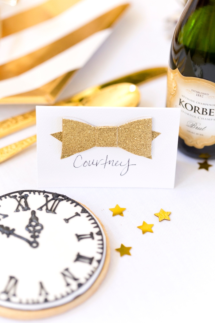 marque place nouvel an en noeud de papillon de papier doré, sablé à motif horloge nouvel an, couverts et assiettes or et blanc