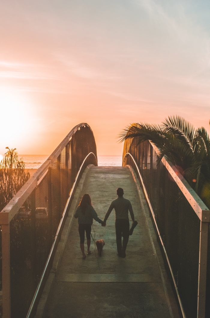 idée d'activite a faire a 2, couple amoureux avec leur chien en promenade au bord de la mer au coucher de soleil