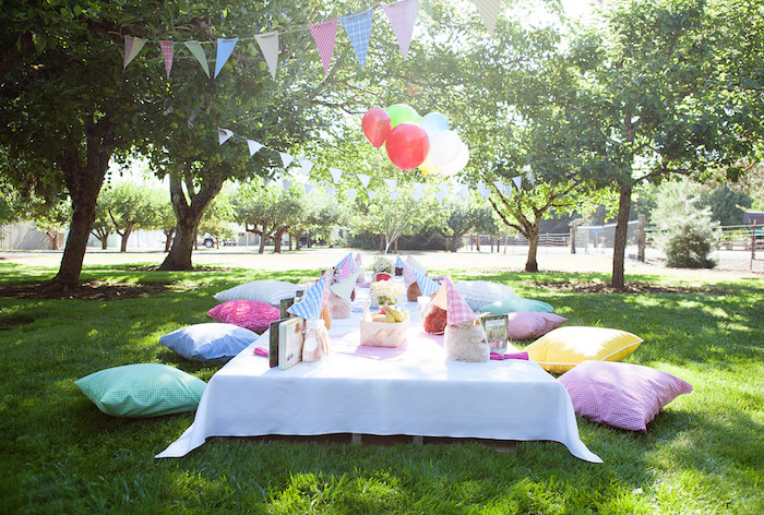 decoration pour anniversaire pc nique en plein aur, table basse avec nappe blanche et serviettes et coussins colorés pat sol