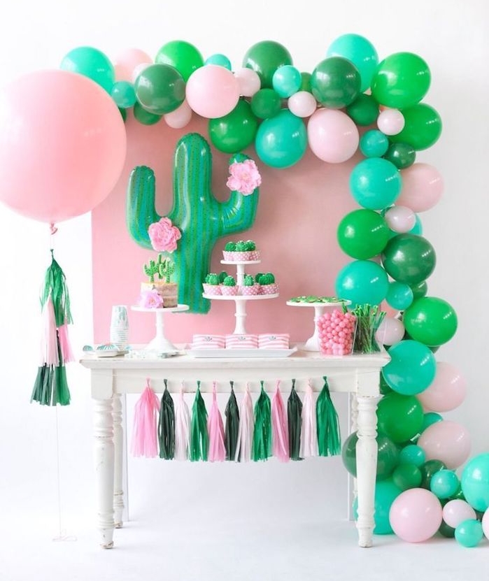 ballons d anniversaire en rose et vert et mur de fond rose, guirlande de pompons rose et vert, idee deco cactus soirée à thème, candy bar anniversaire original